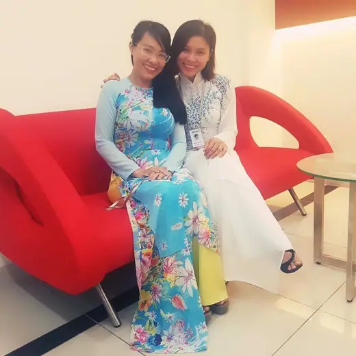Hai phụ nữ mặc áo dài ngồi trên ghế sofa đỏ.