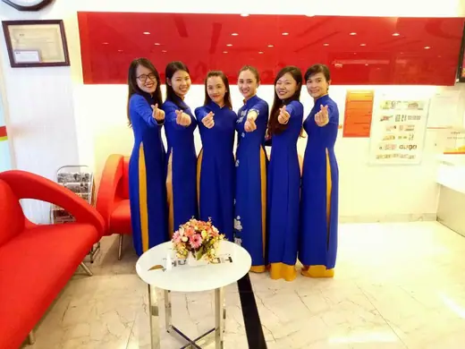 Sáu nữ nhân viên mặc áo dài xanh dương tạo dáng trong sảnh giao dịch.