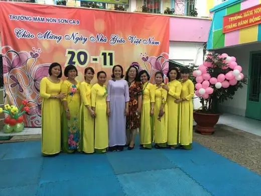 Tập thể cô giáo mặc áo dài vàng đứng trước phông chào mừng ngày Nhà giáo Việt Nam 20-11.