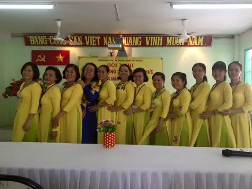 Tập thể cô giáo mặc áo dài vàng đứng thành hàng trong hội trường.