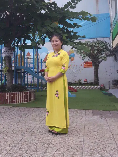 Một cô giáo mặc áo dài vàng thêu hoa đứng ở sân chơi của trường.