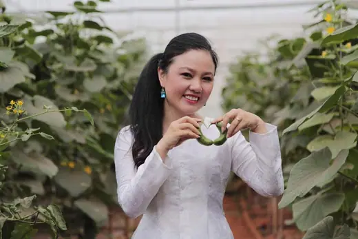 Một phụ nữ mặc áo bà ba trắng đứng giữa vườn cây.