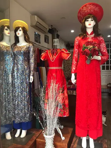 Các ma-nơ-canh trong tiệm mặc áo dài cưới đỏ, đội mấn, cạnh áo gấm và váy đỏ.