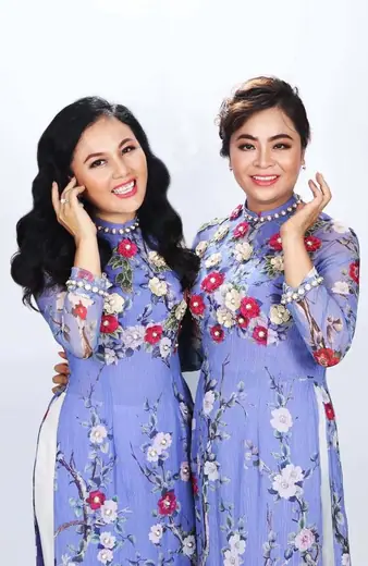 Hai phụ nữ mặc áo dài đôi xanh tím nhạt in hoa trong phòng chụp.
