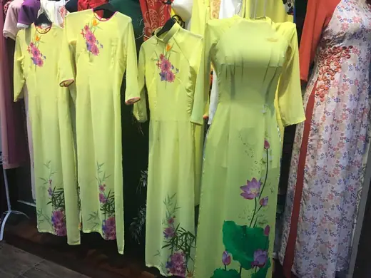 Dãy áo dài đồng phục xanh cốm vẽ hoa sen treo trên sào.