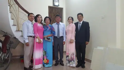 Sáu người trong gia đình, các bà mặc áo dài hồng và xanh, các ông mặc vest, chụp trong nhà ngày đón dâu.