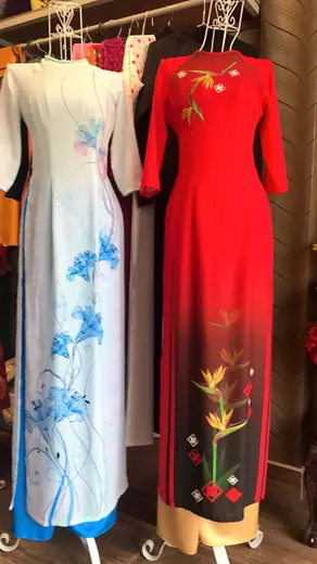 Hai chiếc áo dài trên ma-nơ-canh: một trắng vẽ hoa xanh, một đỏ vẽ hoa thiên điểu.