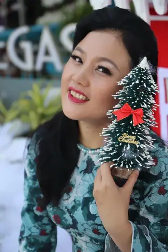 Một phụ nữ mặc áo dài xanh hoạ tiết cầm cây thông nhỏ.