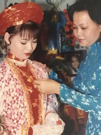 Ảnh cũ: cô dâu đội mấn đỏ được một phụ nữ mặc áo dài gấm xanh đeo trang sức.
