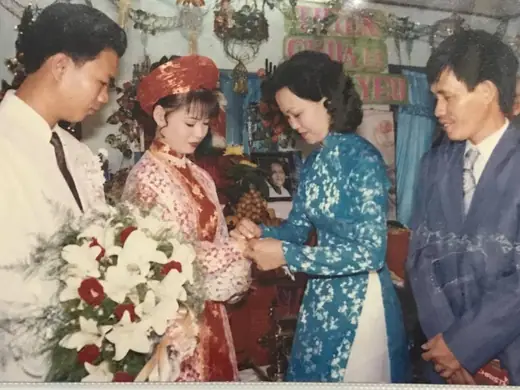 Ảnh cũ: cô dâu ôm bó hoa bên chú rể và người thân trong lễ cưới.