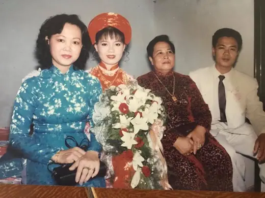 Ảnh cũ: cô dâu đội mấn đỏ ngồi cùng người thân, một phụ nữ mặc áo dài gấm xanh.