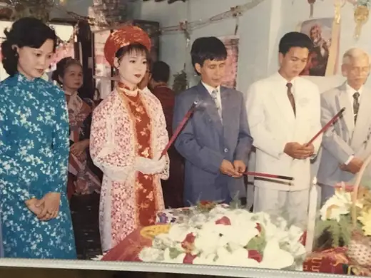 Ảnh cũ: cô dâu mặc áo dài ren đỏ thắp hương cùng chú rể và gia đình trước bàn thờ.