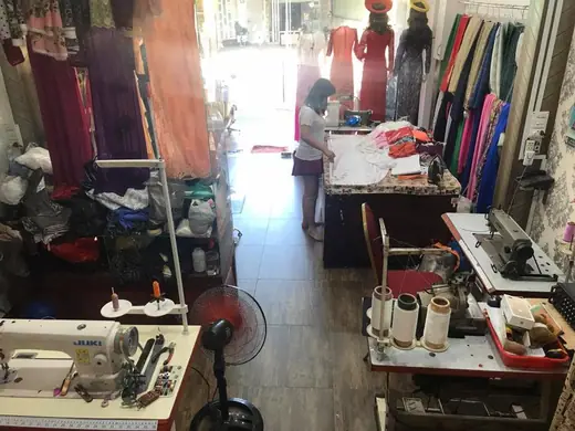 Góc xưởng may của tiệm với máy may, vải vóc và người thợ đang làm việc.