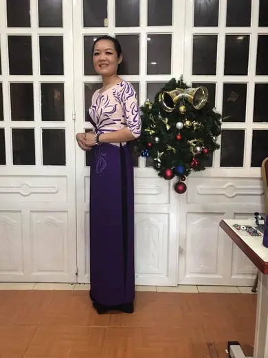 Một phụ nữ mặc áo dài tím phối kem hoạ tiết uốn lượn đứng trong tiệm.
