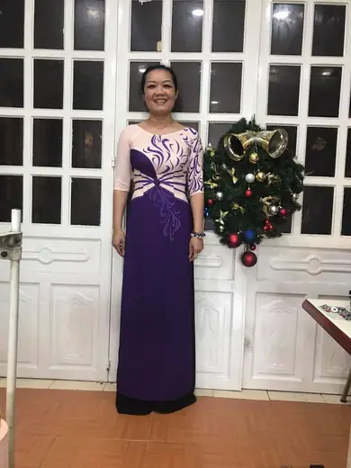 Một phụ nữ mặc áo dài tím phối kem đứng trước cửa kính trong tiệm.