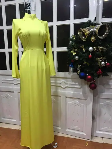 Áo dài vàng chanh trên ma-nơ-canh trước cửa kính treo vòng lá Noel.