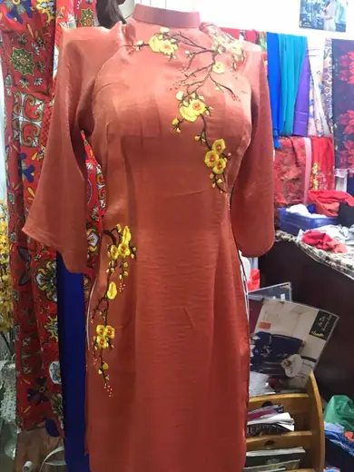 Áo dài màu cam đất thêu hoa mai vàng trên ma-nơ-canh.