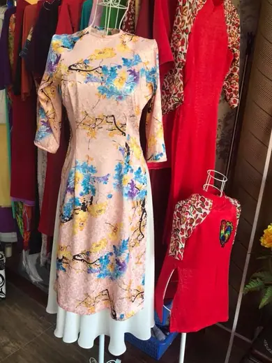 Áo dài cách tân in hoa nền hồng nhạt cạnh áo dài đỏ trẻ em trên ma-nơ-canh.