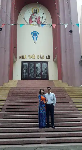 Một đôi nam nữ đứng trên bậc thềm trước nhà thờ, người phụ nữ mặc áo dài.