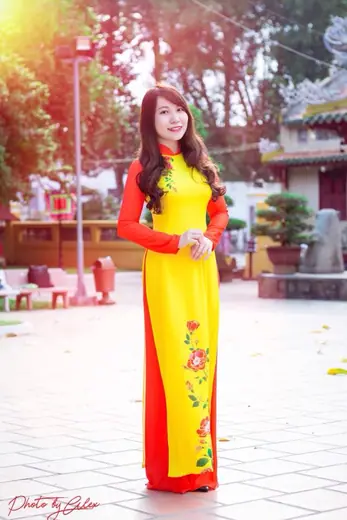 Một cô gái mặc áo dài vàng phối đỏ đứng trong sân chùa.