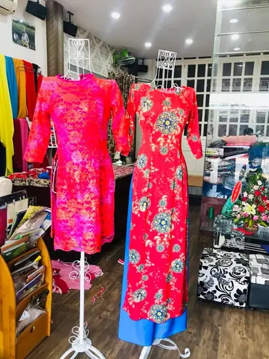 Áo cách tân gấm hồng và áo dài đỏ in hoa trên ma-nơ-canh trong tiệm.