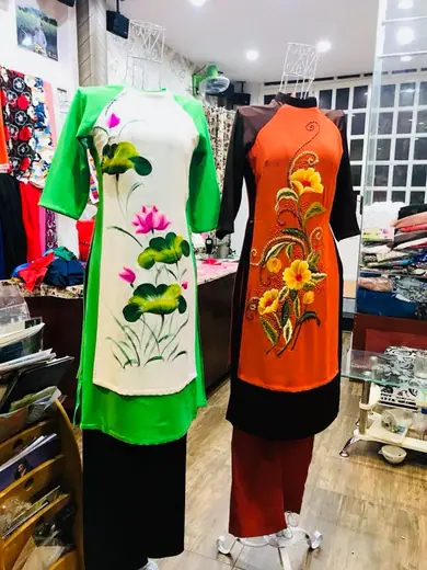 Hai bộ áo cách tân trên ma-nơ-canh: trắng vẽ hoa sen phối xanh lá và cam vẽ hoa phối đen.