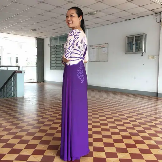 Một phụ nữ mặc áo dài tím phối kem đứng nghiêng trong sảnh lát gạch bông.