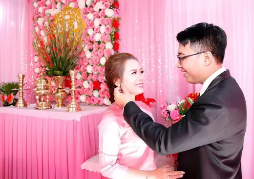 Chú rể mặc vest cài hoa cho cô dâu mặc áo dài hồng trong lễ cưới.