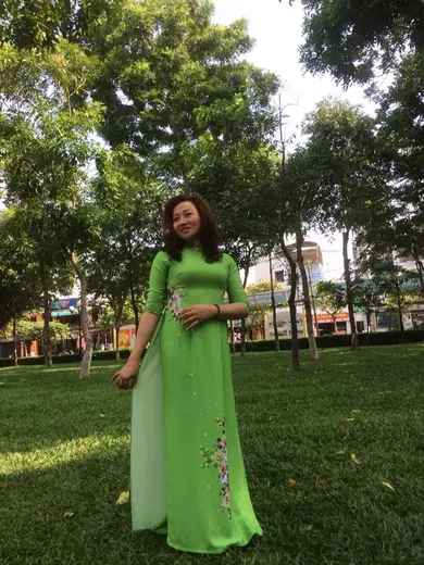 Một phụ nữ mặc áo dài xanh lá đứng trong công viên.
