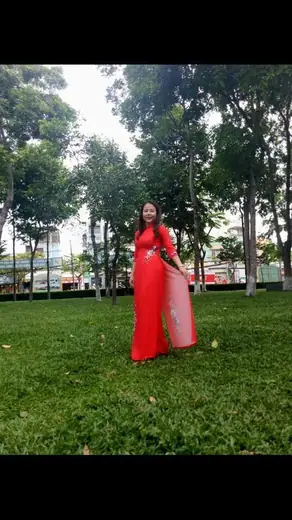 Một phụ nữ mặc áo dài đỏ đứng trên bãi cỏ công viên.