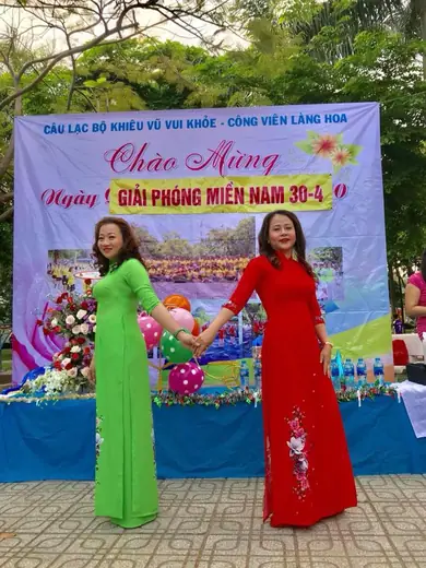 Hai phụ nữ mặc áo dài xanh lá và đỏ nắm tay trước phông câu lạc bộ khiêu vũ chào mừng 30-4.