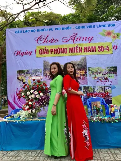 Hai phụ nữ mặc áo dài xanh lá và đỏ đứng trước phông lễ hội ở công viên.