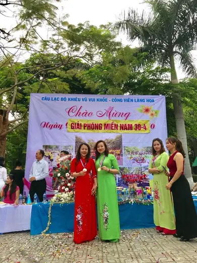 Nhóm phụ nữ mặc áo dài đứng trước sân khấu lễ hội trong công viên.