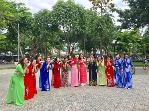 Đông đảo phụ nữ mặc áo dài nhiều màu xếp hàng tạo dáng trong công viên.