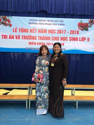 Hai cô giáo mặc áo dài in hoa và áo dài sẫm màu trước phông lễ tổng kết năm học.