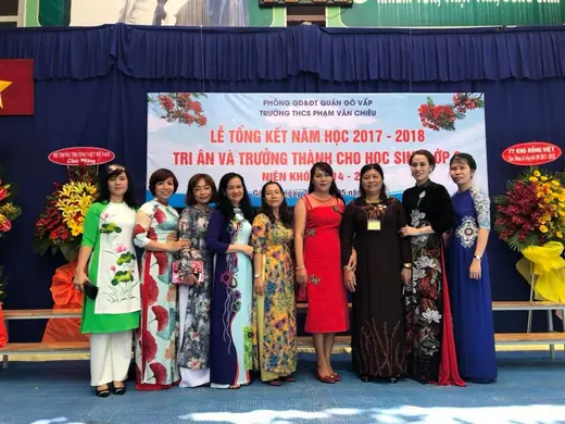 Tập thể cô giáo mặc áo dài chụp chung trước phông lễ tổng kết năm học.