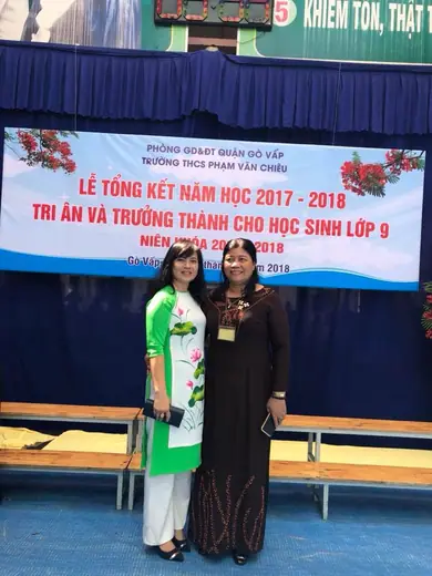 Hai cô giáo mặc áo dài đứng trước phông lễ tổng kết năm học.
