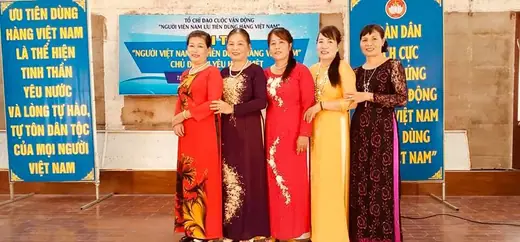 Năm phụ nữ mặc áo dài đứng trên sân khấu một hội thi, hai bên là băng rôn cổ động dùng hàng Việt.