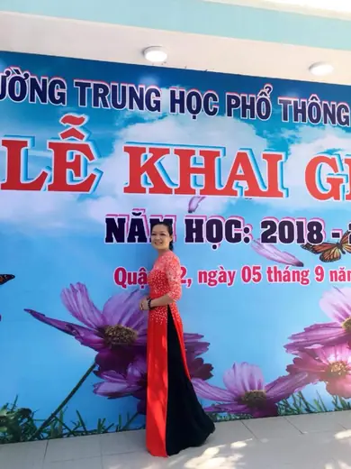 Một cô giáo mặc áo dài đỏ đứng trước phông lễ khai giảng năm học 2018-2019.