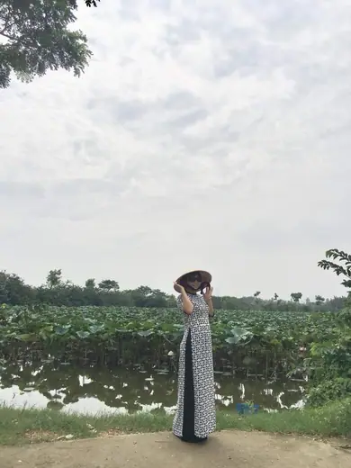 Một cô giáo mặc áo dài, đội nón lá, đứng bên đầm sen.