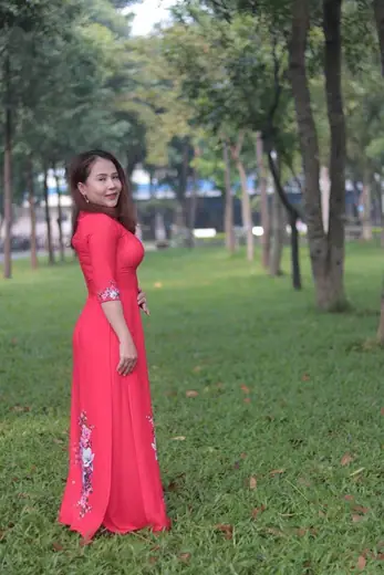 Một phụ nữ mặc áo dài đỏ san hô đứng trên bãi cỏ công viên.