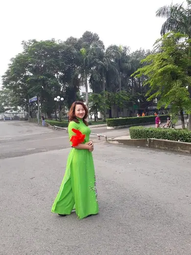 Một phụ nữ mặc áo dài xanh lá cầm quạt đứng giữa sân.