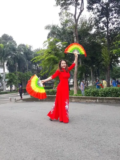 Một phụ nữ mặc áo dài đỏ múa hai chiếc quạt nhiều màu.