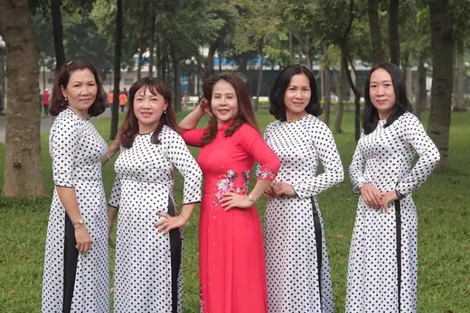 Năm phụ nữ, bốn người mặc áo dài trắng chấm bi và một người áo dài hồng, trong công viên.