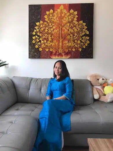 Một phụ nữ mặc áo dài gấm xanh ngồi trên sofa xám.