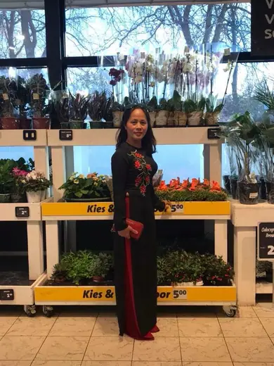 Một phụ nữ mặc áo dài đen thêu hoa đứng trong một cửa hàng cây cảnh.