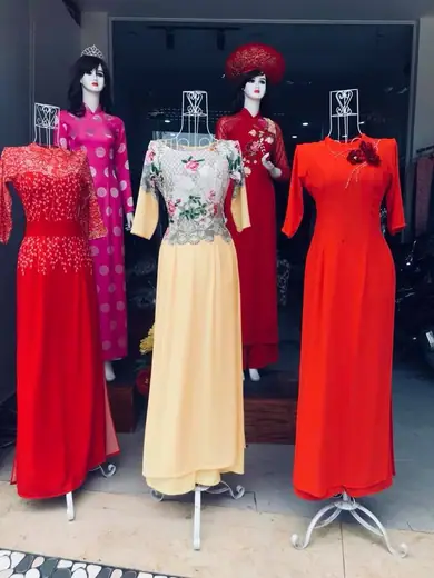 Bốn ma-nơ-canh trong tiệm mặc áo dài đỏ kết cườm, áo ren phối chân váy kem, áo dài cưới đỏ đội mấn và áo dài đỏ cam.