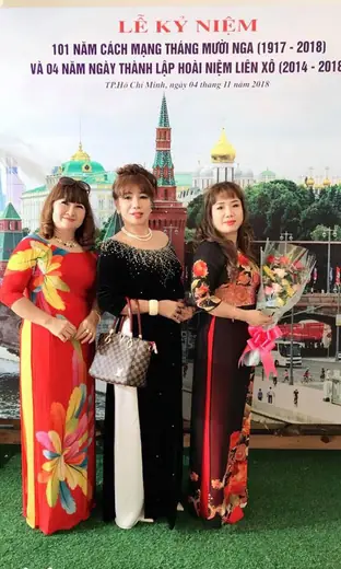 Ba phụ nữ mặc áo dài đứng trước phông lễ kỷ niệm Cách mạng tháng Mười Nga.