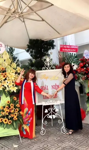 Hai phụ nữ mặc áo dài tạo dáng bên bảng hiệu sự kiện.