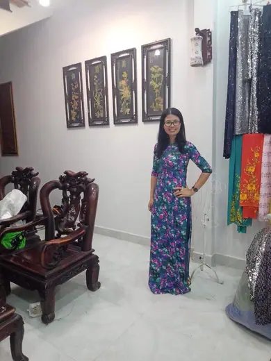 Một cô giáo mặc áo dài lụa in hoa tối màu đứng trong phòng khách.